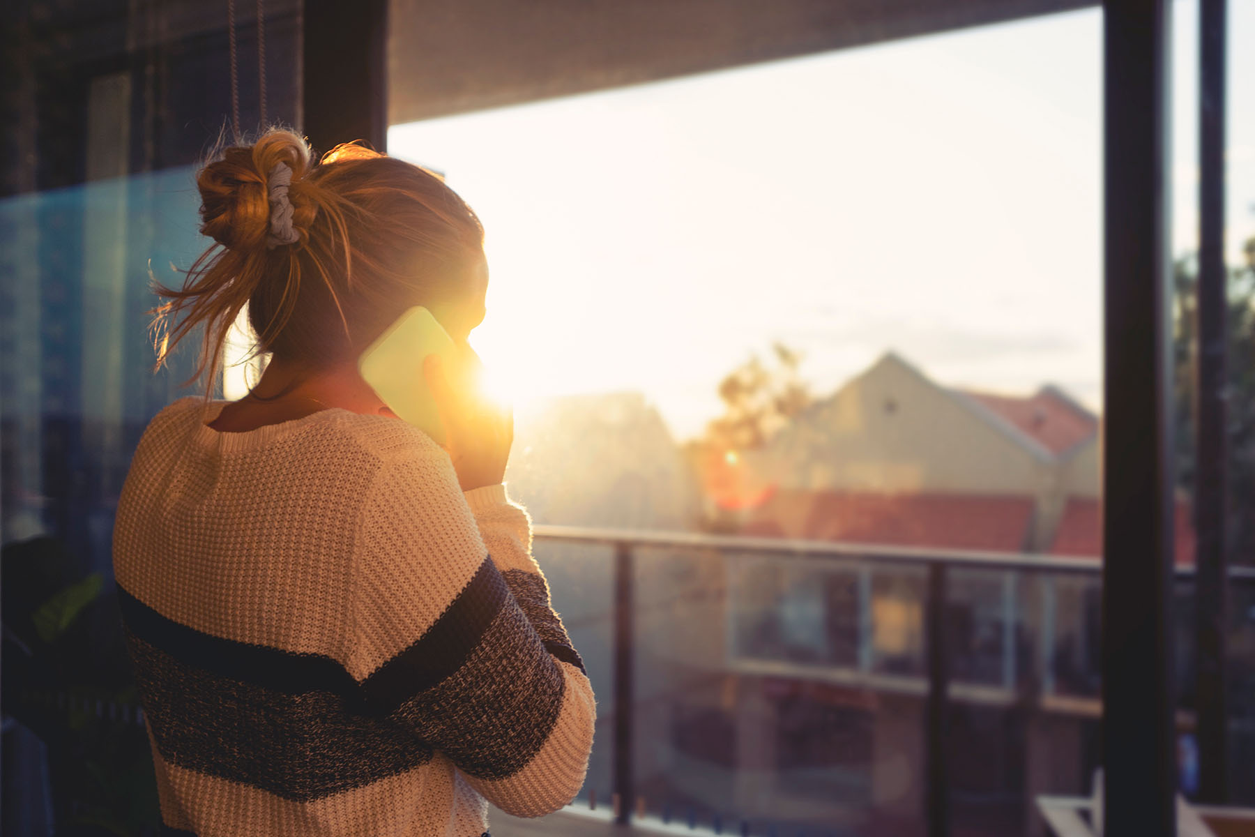 A lady on the phone looking out from a balcony window